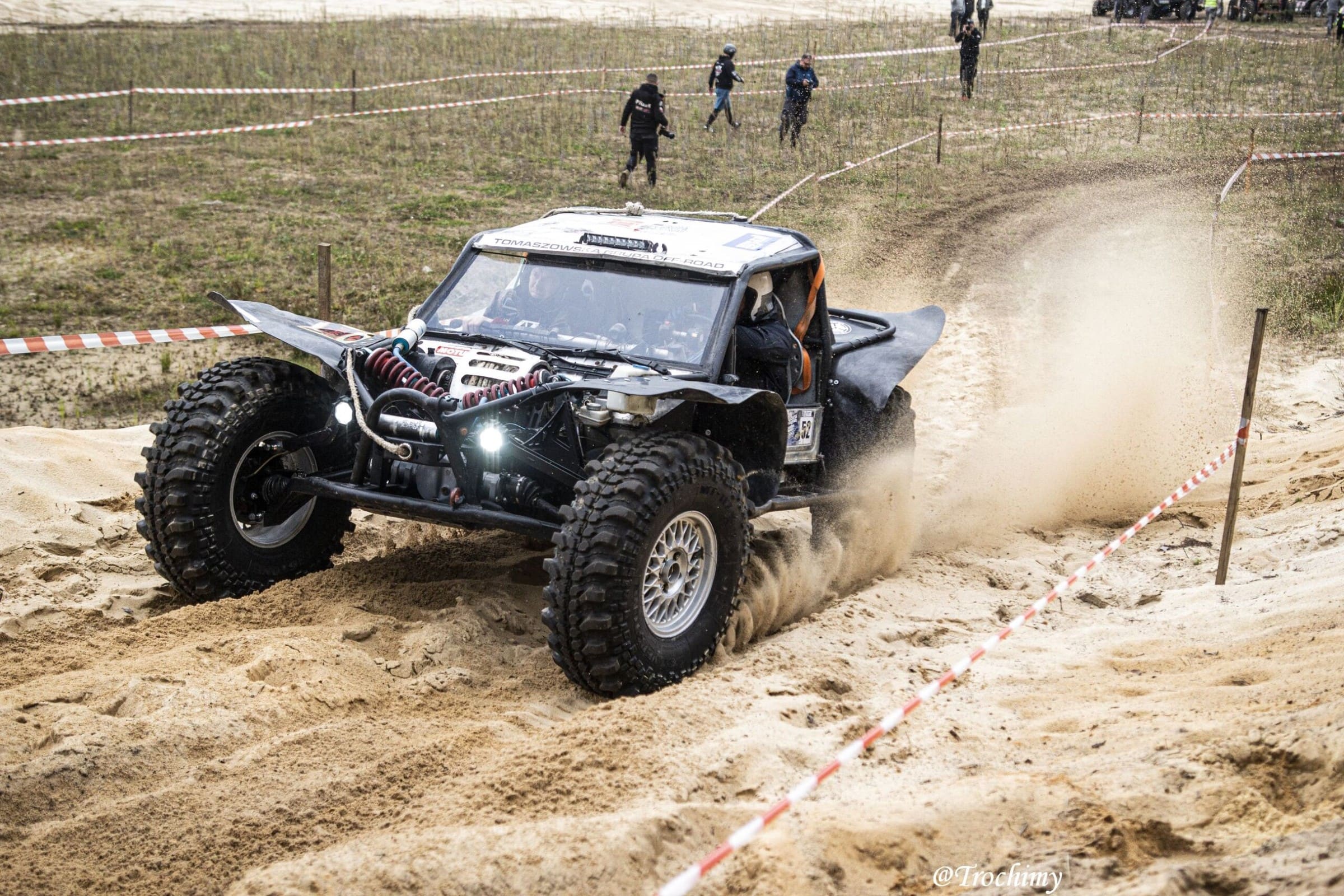 Czarny buggy w piachu, taśmy trasy, kibice w tle