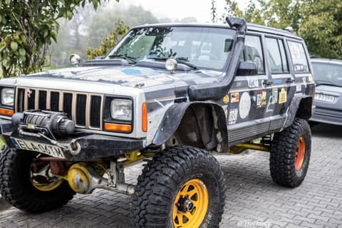 Srebrny Jeep Cherokee z wyciągarką, snorkelem i żółtymi felgami na parkingu