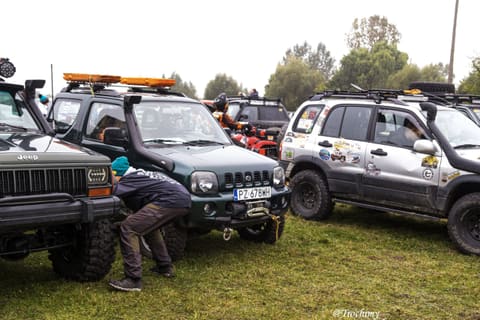 Uczestnik schyla się przy wyciągarce zielonego Suzuki Jimny między terenówkami