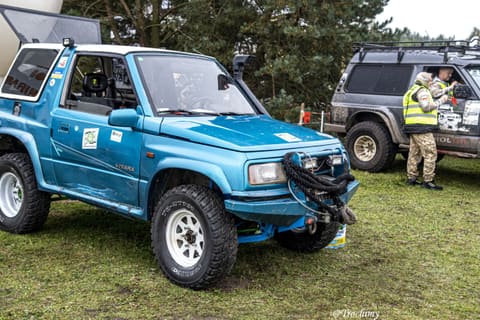Turkusowa Suzuki Vitara z wyciągarką na trawie, w tle porządkowy