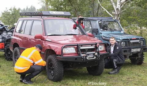 Mechanik spuszcza powietrze z opony czerwonej Suzuki Vitary, obok uśmiechnięty kierowca