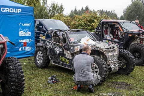Mężczyzna kuca przy kole zniszczonego buggy Virus obok namiotu sponsora