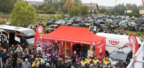 Tłum uczestników przy czerwonym namiocie sponsora, w tle pole terenówek