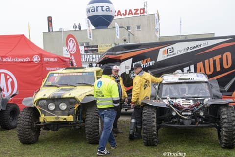 Załogi rozmawiają przy żółtym i czarnym buggy przed ciężarówką serwisową
