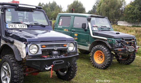 Granatowe Suzuki Samurai i zielone Samurai na pomarańczowych felgach na trawie