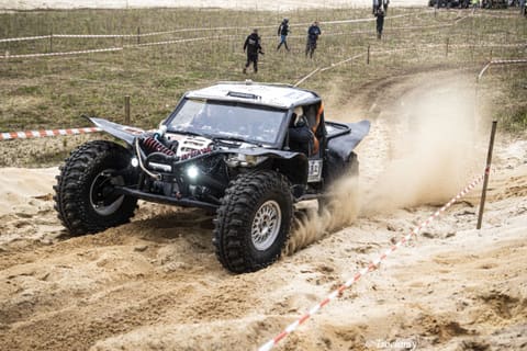 Czarne buggy wyrzuca piach, pokonując piaszczysty zakręt trasy wyznaczonej taśmą