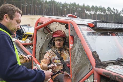 Sędzia ze stoperem podaje kartę zawodniczce w czerwonym kasku w klatce buggy