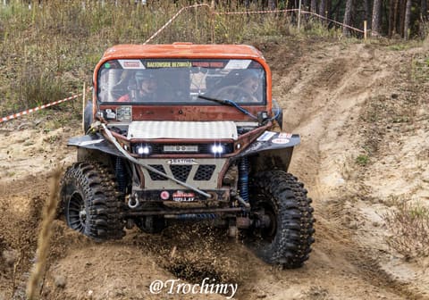 Pomarańczowy buggy z załogą zjeżdża prosto na obiektyw w piaszczystym wąwozie