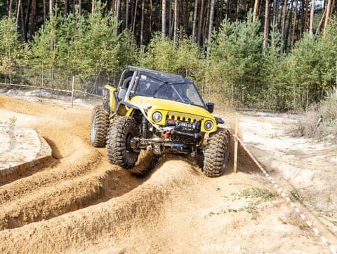 Żółty buggy pokonuje głębokie koleiny w piasku na tle sosnowego lasu