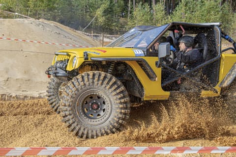 Żółty buggy z bliska sypie piaskiem spod kół, kierowca w kasku widoczny