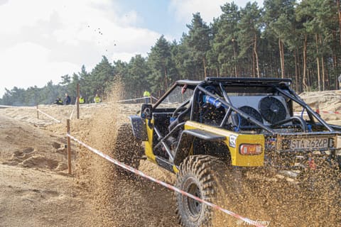 Żółto-czarny buggy od tyłu wyrzuca fontannę piasku na zakręcie trasy