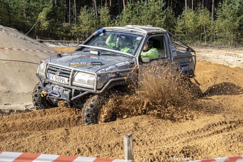 Srebrny pick-up terenowy z klatką przebija się przez piach w chmurze piasku
