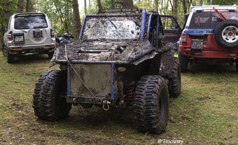 Oblepiony błotem niebieski buggy z wyciągarką stoi na trawie między terenówkami