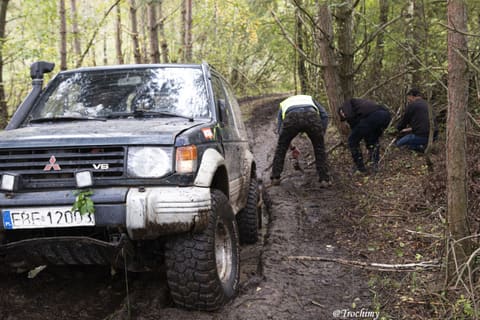 Mitsubishi Pajero w leśnej koleinie, obok załoga kopie i podkłada gałęzie