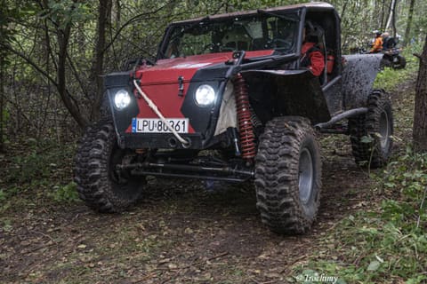 Czerwono-czarny buggy z zapalonymi reflektorami jedzie wąską leśną ścieżką