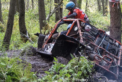 Pilot wspina się na klatkę przechylonego pomarańczowego buggy w leśnym błocie