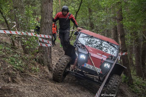 Czerwony buggy zjeżdża na linie stromym leśnym zboczem, obok schodzi pilot