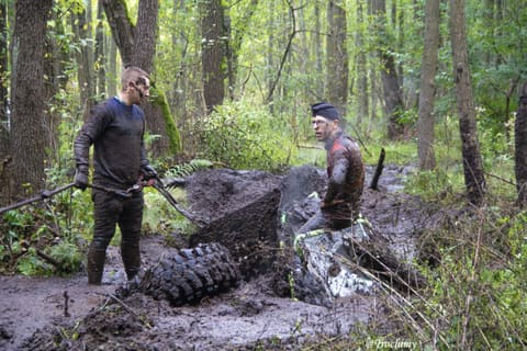 Dwóch oblepionych błotem zawodników walczy z przewróconym buggy w leśnym bagnie