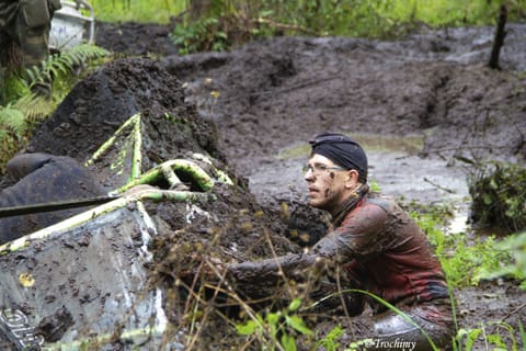 Zawodnik w okularach i chuście, cały w błocie, przy klatce przewróconego buggy