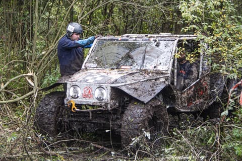 Zawodnik w kasku przy zabłoconym białym buggy w gęstych leśnych zaroślach