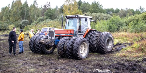 Ciągnik Massey Ferguson na podwójnych kołach na podmokłej łące, obok grupa osób
