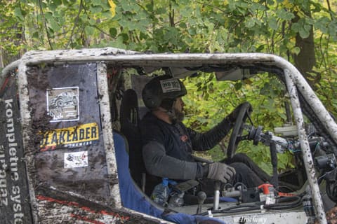 Kierowca w kasku za kierownicą zabłoconego buggy, widok przez klatkę