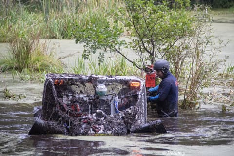 Zatopiony po dach zabłocony buggy w stawie, obok zawodnik brodzi w wodzie