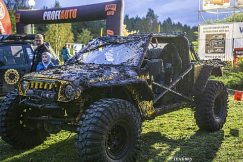Czarno-żółty buggy pokryty błotem przed bramą w bazie zawodów, obok widzowie