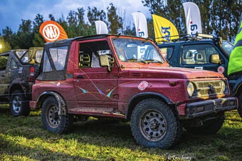 Czerwone Suzuki Samurai ochlapane błotem stoi na trawie w bazie zawodów