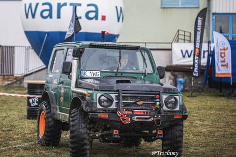 Zielone Suzuki Samurai z wyciągarką i pomarańczowymi felgami w bazie zawodów