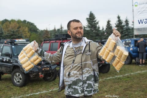 Uśmiechnięty mężczyzna w moro bluzie trzyma dwa worki bułek w parku maszyn