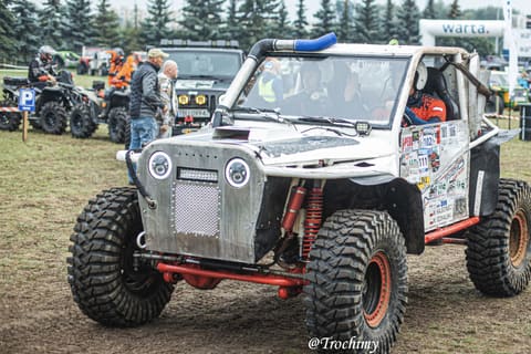 Srebrny buggy z czerwoną ramą i ogromnymi oponami wyjeżdża na plac startowy