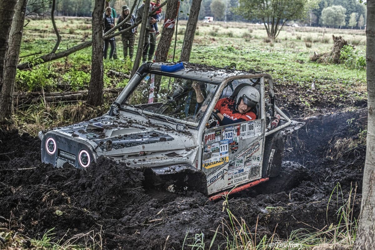 Srebrny buggy z kierowcą w kasku grzęźnie w leśnym błocie