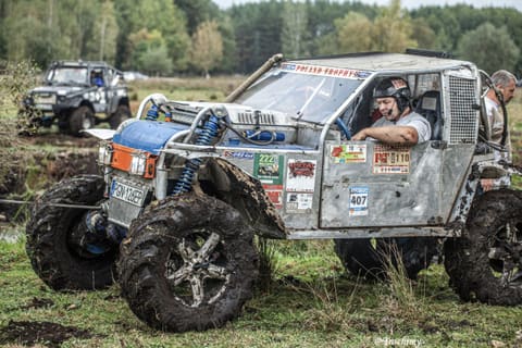 Kierowca srebrnego buggy wychyla się z kabiny podczas przejazdu przez błotnistą łąkę