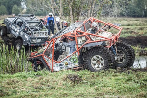 Przechylony buggy z pomarańczową klatką w rowie z wodą, za nim druga terenówka