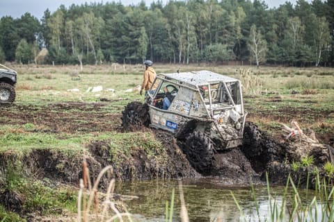 Buggy z klatką wspina się z rowu wypełnionego wodą na podmokłej łące