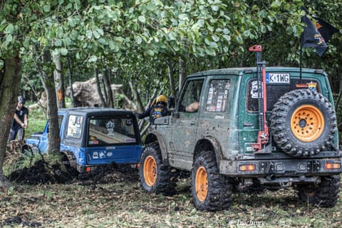 Zielony i niebieski Suzuki w leśnym błocie, kierowca wychyla się z kabiny