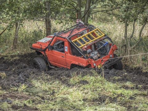 Pomarańczowy Suzuki z żółtą drabiną w klatce grzęźnie w błocie na lince wyciągarki