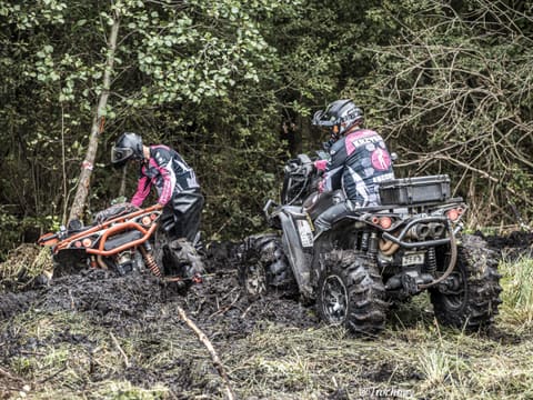 Dwóch zawodników na quadach przepycha się przez błoto w zaroślach