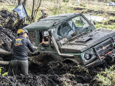 Zielony Suzuki zakopany głęboko w błocie, pomocnik w kasku rozmawia z kierowcą