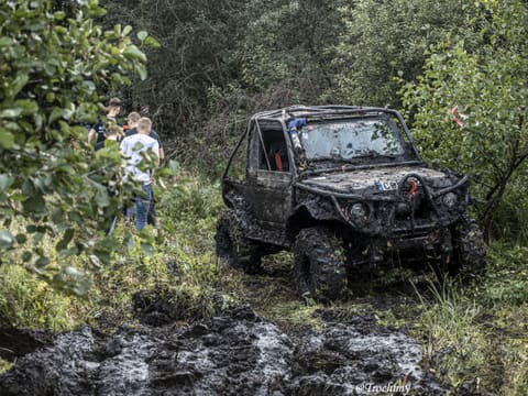 Czarny zabłocony Suzuki z klatką wyjeżdża z leśnego błota, obok widzowie