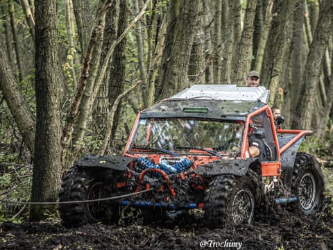 Pomarańczowo-czarny buggy z niebieskimi sprężynami na lince wyciągarki w leśnym błocie