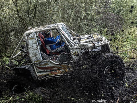 Biały buggy z kierowcą w niebieskim kombinezonie rozrzuca błoto w lesie