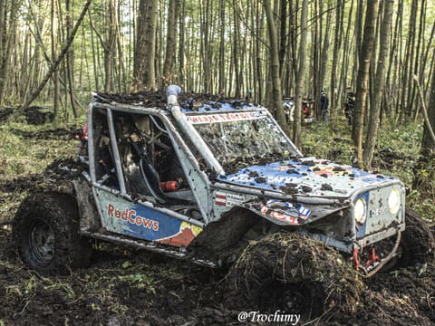 Biało-niebieski buggy z rurową klatką brnie przez błoto w lesie