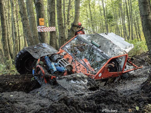 Pomarańczowy buggy z rurową klatką mocno przechyla się w głębokim błocie leśnego odcinka