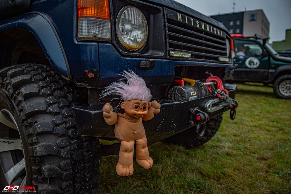 Plastikowy troll z różowymi włosami przyczepiony do zderzaka granatowego Mitsubishi