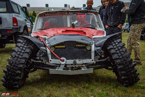 Przód srebrno-czerwonego buggy na dużych oponach terenowych w bazie wśród uczestników