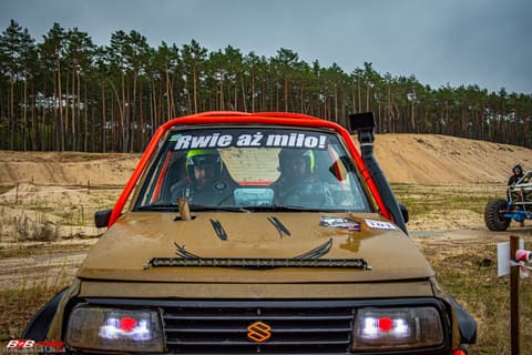 Brązowe Suzuki Vitara z napisem Rwie aż miło na szybie przy piaszczystej trasie