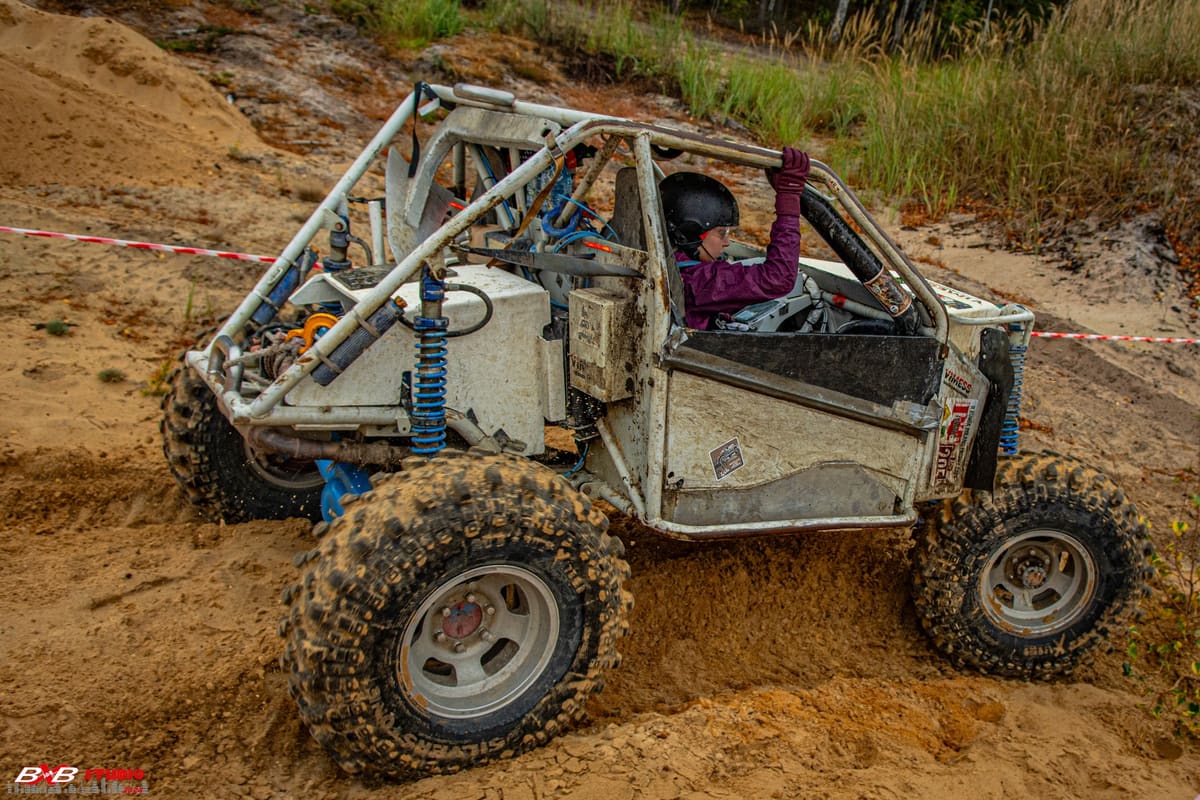 Biały buggy z rurową klatką zjeżdża po piaszczystej skarpie, kierowca macha ręką