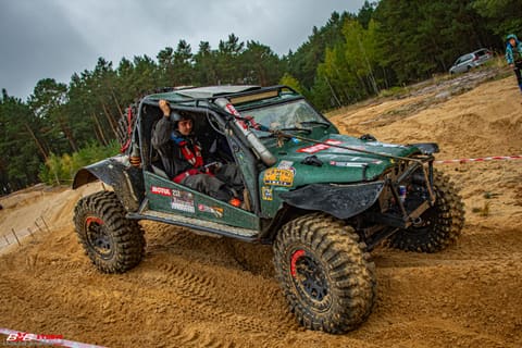 Zielony buggy z klatką pokonuje piaszczystą skarpę, widoczny kierowca w kasku